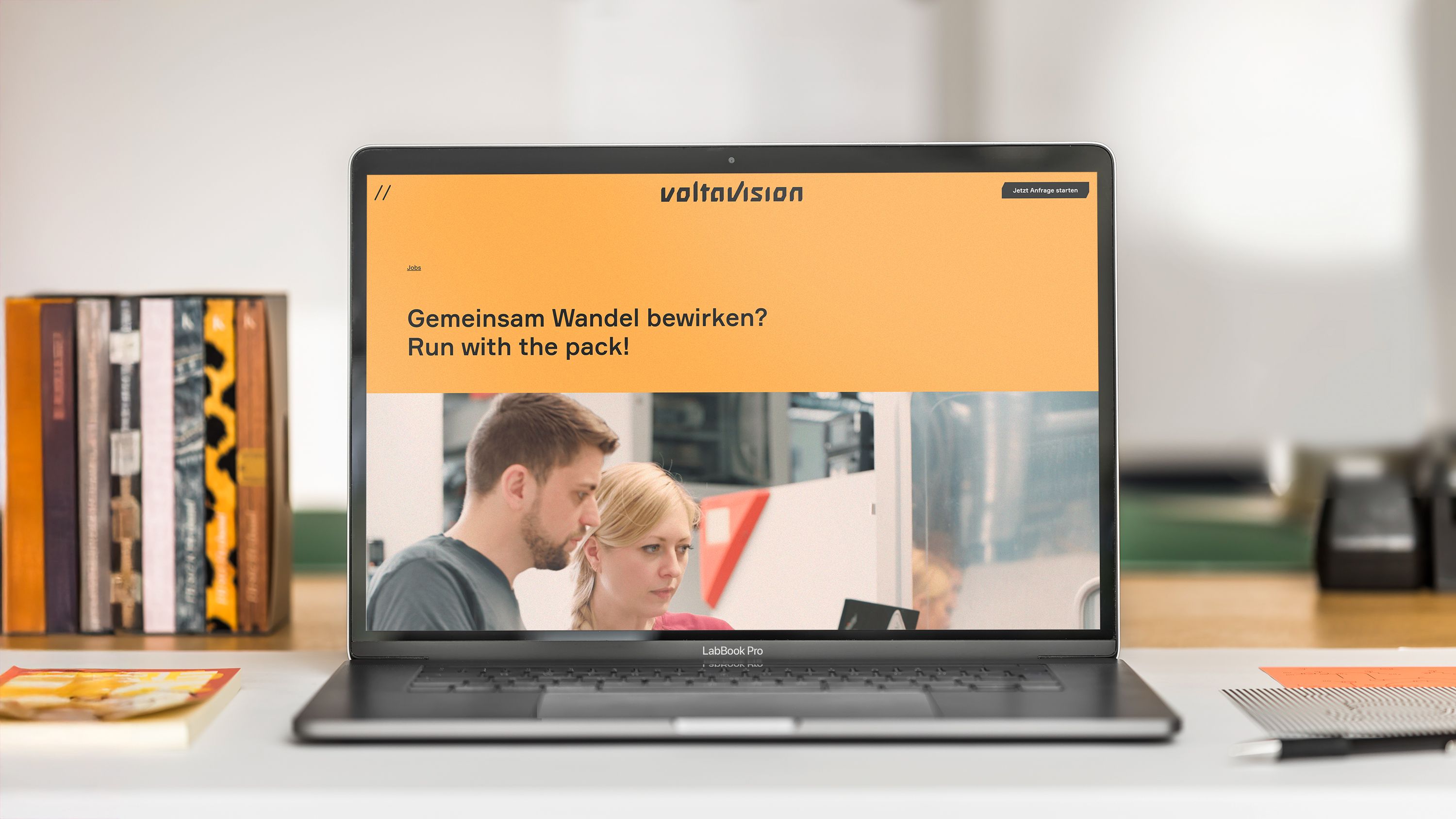 Die Voltavision-Website auf einem Laptop-Screen. Zu sehen ist ein kräftig-gelber Header mit der Überschrift „Gemeinsam Wandel bewirken? Run with the pack!“ und einem Foto von zwei Mitarbeitenden.