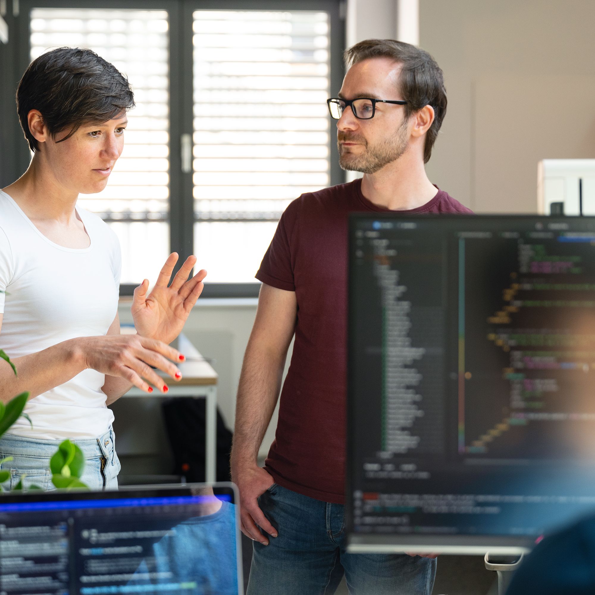 Drei Web-Entwickler:innen von Labor b im fachlichen Dialog. Im Bildvordergrund sind Screens mit Code zu sehen.